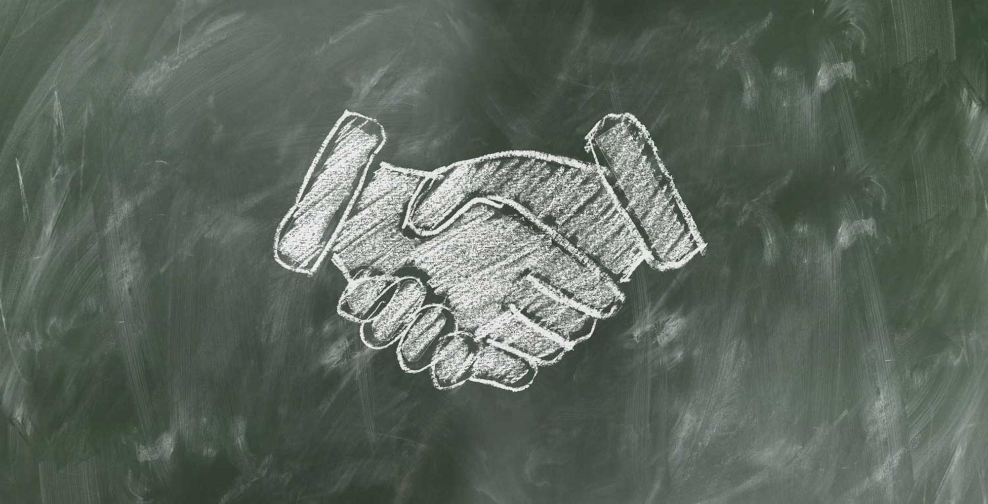 Zwei Hände im Handschlag vor grünem Hintergrund, symbolisch für Zusammenarbeit oder Einigung