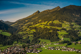 Kleinstadt im Tal, umgeben von grünen Feldern, Wäldern und Bergen mit Felsgipfeln unter klarem, blauem Himmel.