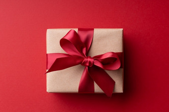 Geschenkbox in braunem Papier mit roter Schleife auf rotem Hintergrund